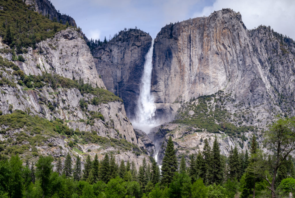Yosemite Falls flowing fully with mountains and trees. Yosemite National Park. About Slow the Parks